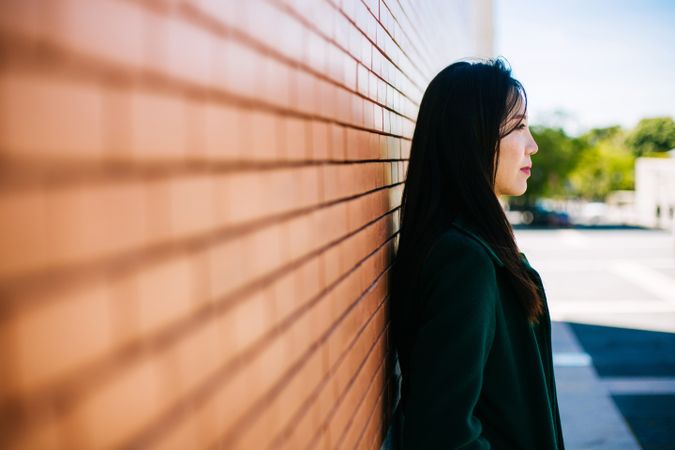 Pensive Asian woman leaning on brick wall