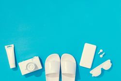 Summer objects of flip flops, sunglasses, camera, smart phone, EarPods on blue background
