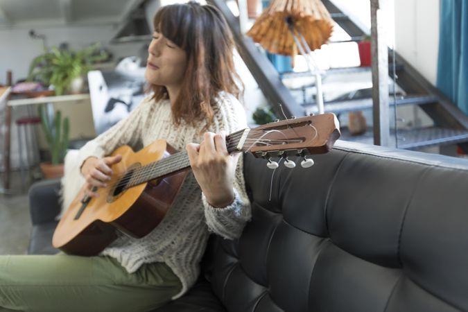 Female on sofa playing acoustic guitar at home in her living room