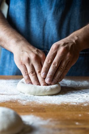 Crop man flattening dough for pizza
