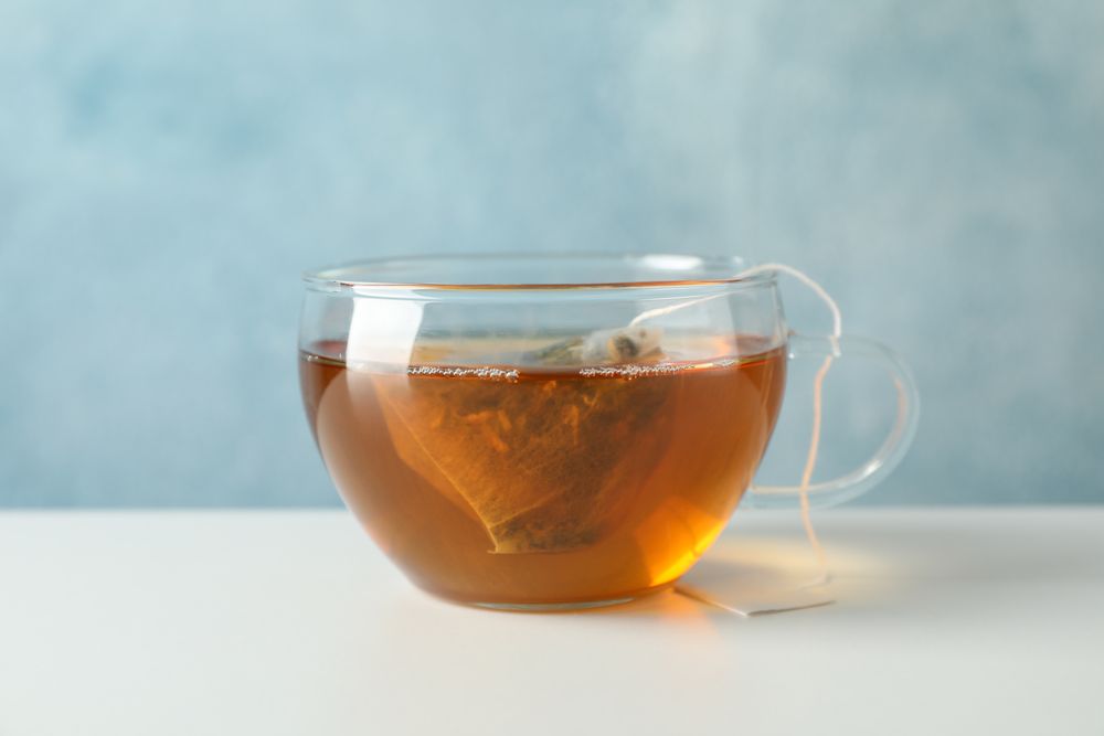 Cup of tea with tea bag on plain background, space for text