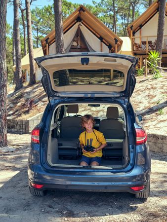 Boy sitting in car trunk and holding binoculars