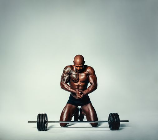 Muscular man working out kneeling in front of heavy weights