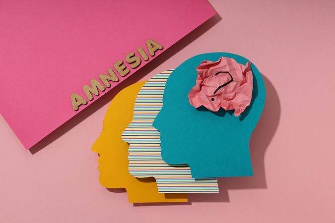 Paper cut outs of colorful head on pink background with the word “Amnesia”