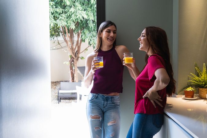 Cheerful women drinking orange juice in modern kitchen