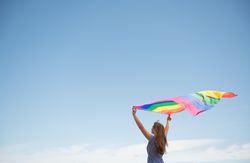 Young woman with rainbow banner against sky
