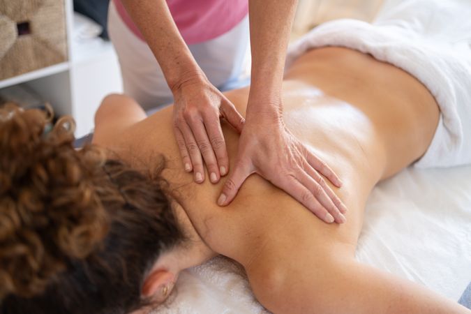 Crop of female masseuse kneading back of client in hospital room