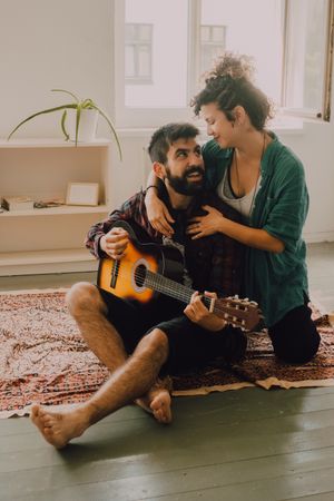 Cheerful couple playing guitar at home
