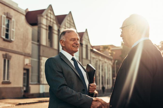 Two business partners handshake outdoors with a sun flare