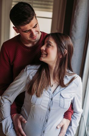 Pregnant woman with husband looking at window at home
