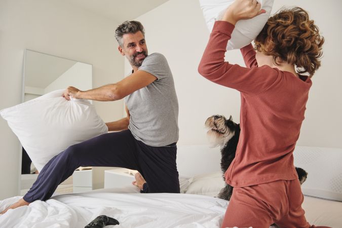 Happy man and boy fighting with pillows on bed
