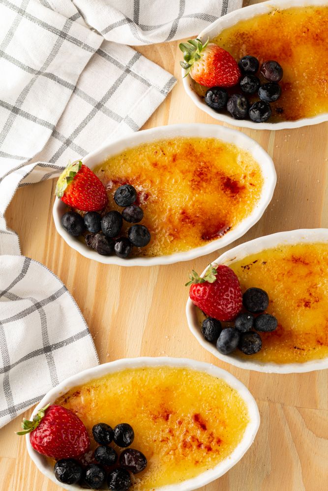 Top view of ramekins of creme brûlée with berries on wooden table