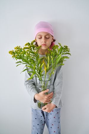 Serene kid in bandana with goldenrods in vase near wall