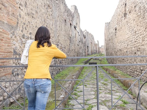 Rear view of a woman in yellow clothes leaning on metallic fence while exploring ancient ruins