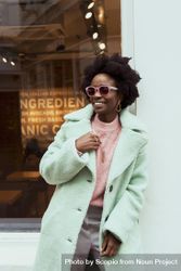 Smiling woman in teal coat wearing sunglasses standing outdoor 0P9zN5