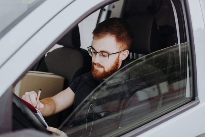 Courier filling papers while preparing for delivery of order to client in car