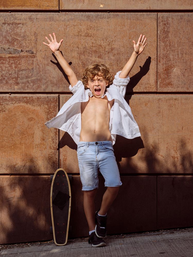 Excited boy with raised arms on street near skateboard