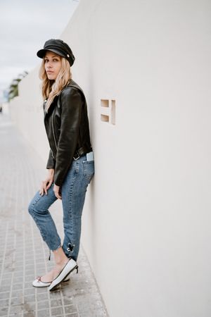 Stylish woman confidently leaning on white wall