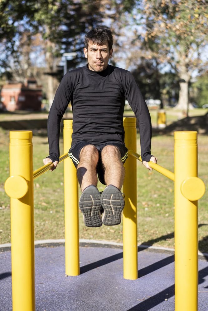 Front view of a young man doing abdominal exercises on a public equipment in outdoor fitness