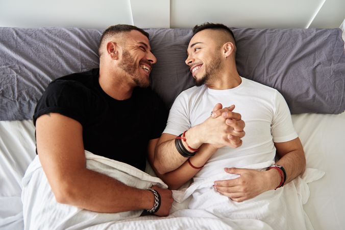 Smiling gay couple hugging on bed