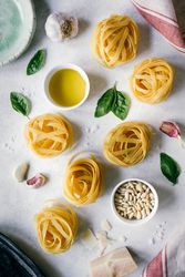 Nests of tagliatelle pasta with basil leaves and garlic on table