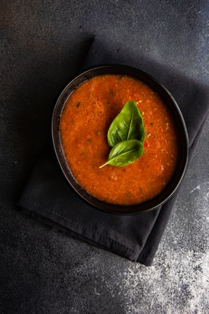 Top view of dark bowl of gazpacho soup with basil leaves