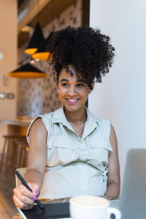 Smiling Black woman working on graphic tablet in cafe