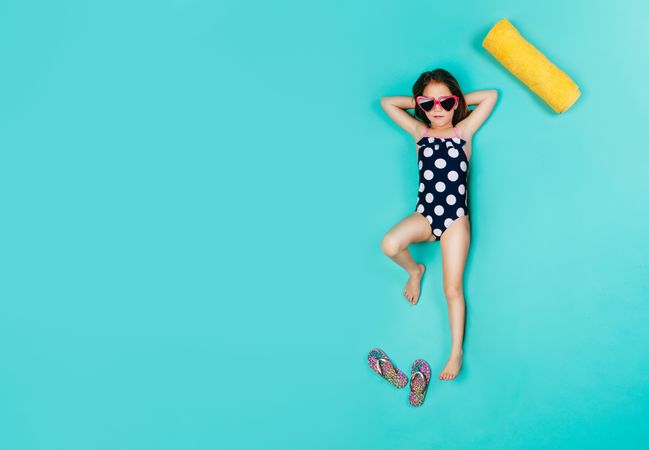 Top view of girl wearing swimwear and sunglasses lying on blue background
