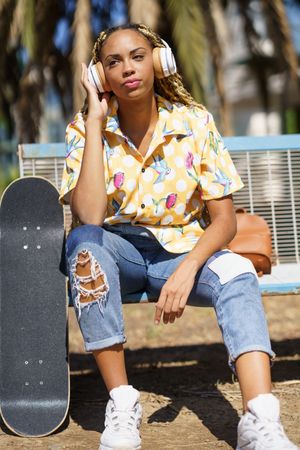 Female in bold patterned shirt sitting on park bench listening to music on large headphones