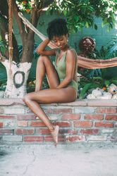 Woman model sitting on garden wall with one leg up looking down
