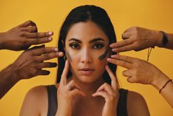 Latina woman with different hands outreaching to apply mud mask