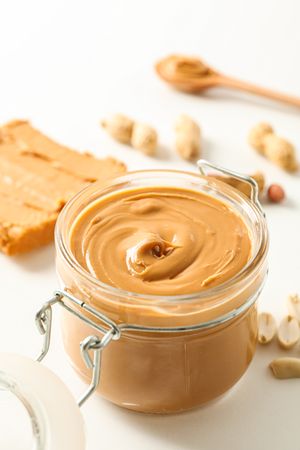Composition with peanut butter sandwich, glass jar, peanut and spoon on light background, space for text and closeup