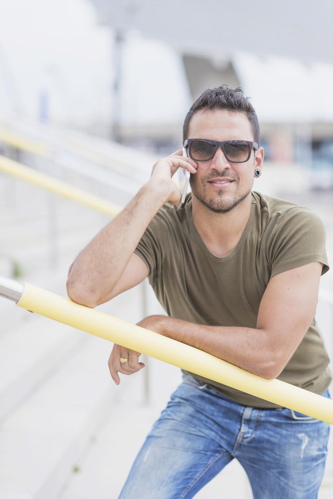 Male standing on stairs outside holding yellow rail and speaking on phone