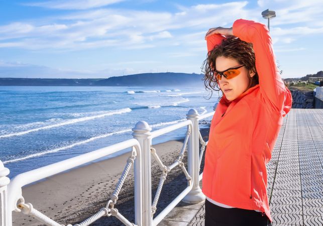 Athletic woman stretching triceps before running on the beach promenade on a summer morning