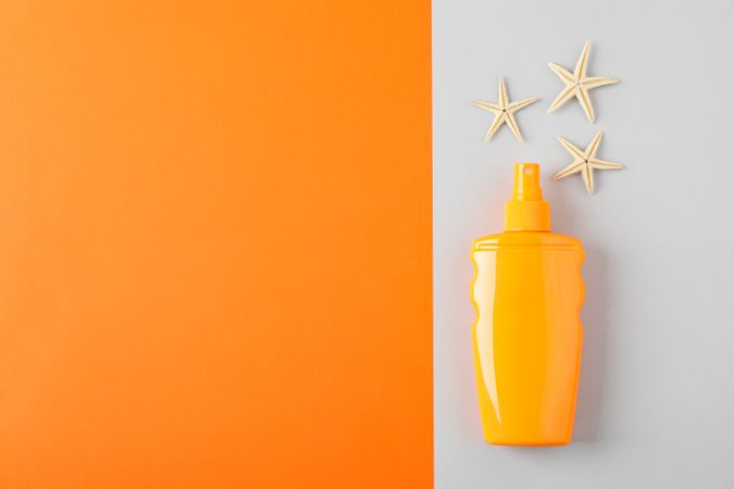 Composition with sunscreen spray and starfishes on two tone background, space for text. Summer vacation backdrop
