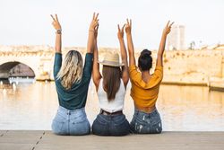 Back of women sitting on riverbank with arms up