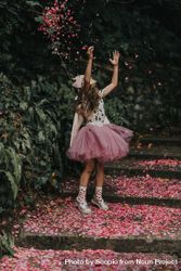 Girl in pink tutu standing on pink petals on ground beside trees 4dk8d5