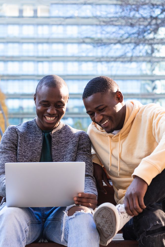 Smiling Black men using laptop while sitting on bench