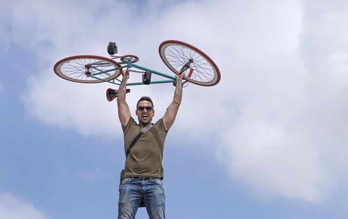 Strong male holding up bike with blue sky and clouds in background