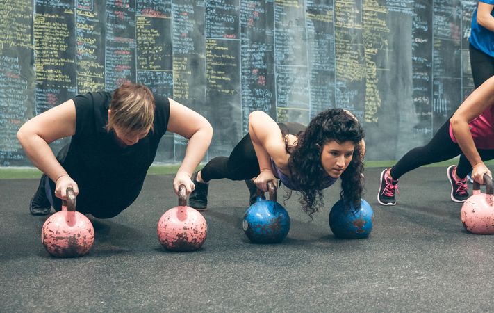 Sportswomen doing push-ups with kettlebells