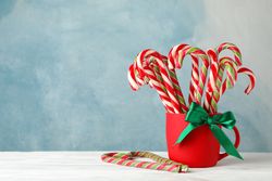 Candy canes in red cup on blue wooden background, space for text