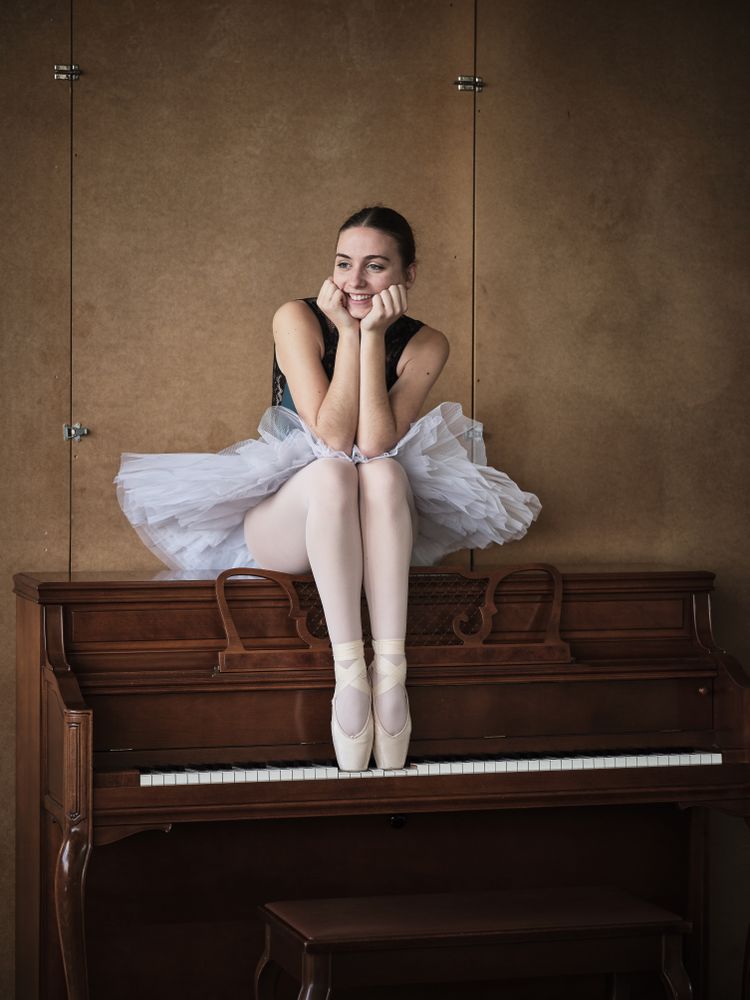 Positive ballerina sitting on piano in pointe shoes