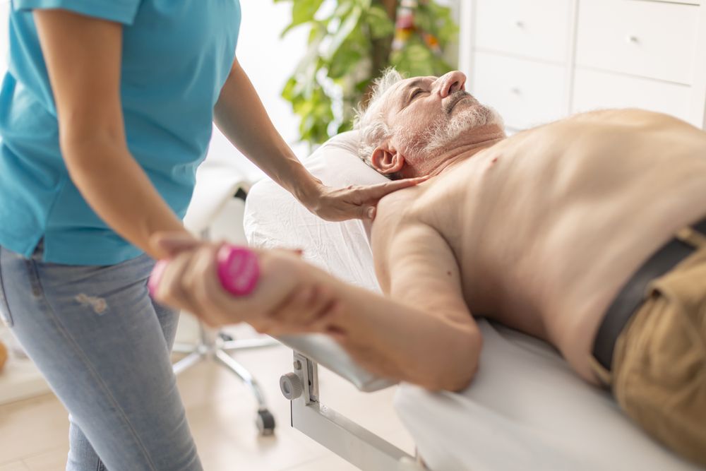 An older man receives a physiotherapy session, using light weights, to treat a problem in his wrist and arm joint