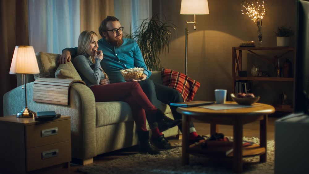In the Evening Man and Woman are Sitting on the Sofa Watching TV and Eating Popcorn.