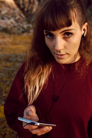 Young woman with piercing listening music on smartphone on hill