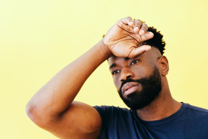 Portrait of Black man in navy t-shirt with one hand to his forehead