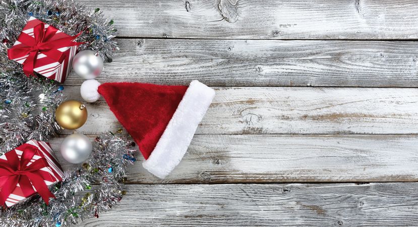 Traditional gold and silver balls, Santa cap plus gifts surrounded by tinsel on a wood background for the Christmas or New Year holiday season