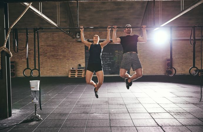 Two fit people doing intense workout using a pull-up bar