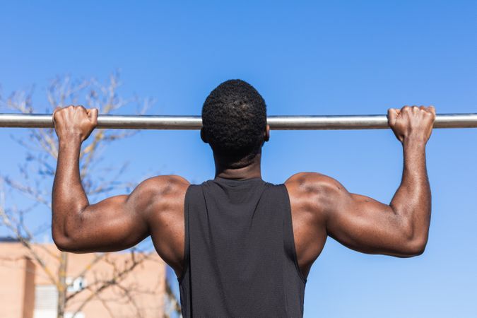 Unrecognizable strong Black sportsman working out on bar in town