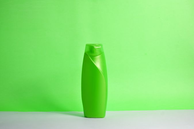 Green body wash bottle with no labels on counter with green background